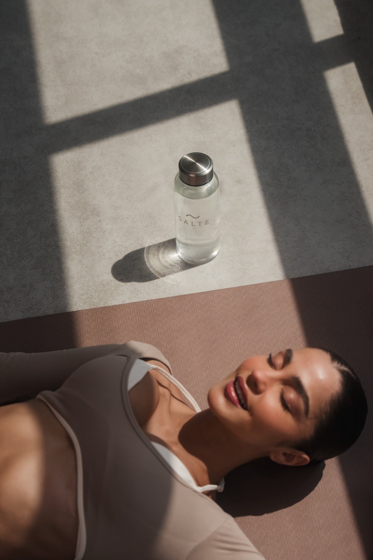 Woman resting on a mat in the sun next to a SALTE bottle