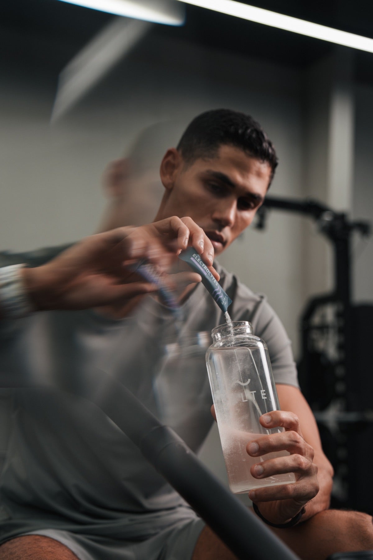 Hombre vertiendo un sobre de SALTE en una botella de agua en el gimnasio